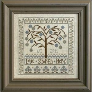 May include: A cross-stitch embroidery design featuring a stylized tree with blue flowers and leaves. The text "Love Spoken Here" is stitched below the tree.