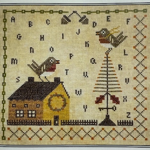 Könnte beinhalten: Kreuzstich-Stickmuster mit einem Haus, einem Baum und zwei Vögeln. Das Haus ist gelb mit einem braunen Dach und einem Kranz an der Tür. Der Baum ist braun mit roten Akzenten. Die Vögel sind braun und rot. Das Stickmuster hat einen beigen Hintergrund und eine dekorative Bordüre.