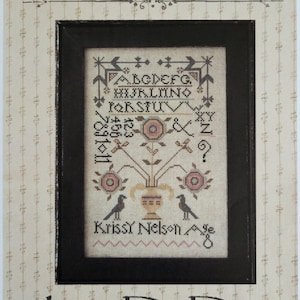 May include: A cross-stitch pattern featuring a floral arrangement with birds and the text "La-D-Da designs for counted thread". The pattern includes an alphabet, numbers, and symbols.