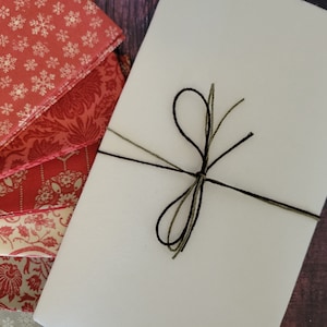 May include: A white envelope tied with black and green twine. The envelope is surrounded by red and white patterned fabric.
