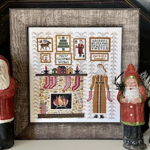 May include: A framed cross-stitch sampler with a Christmas theme. The sampler features a fireplace, stockings, and the text "Merry Christmas Wishes" and "And to all a Goodnight". Two Santa Claus figurines flank the frame.
