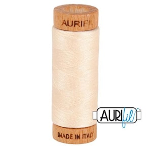 May include: A spool of off-white thread with a wooden bobbin. The bobbin has the text "Aurifil" and "Made in Italy" printed on it.