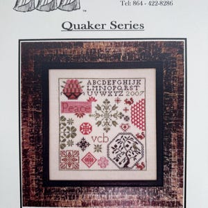 May include: A framed cross-stitch sampler from the "Quaker Series" with the word "Peace" prominently displayed. The sampler features a variety of stitched patterns, including floral and geometric designs, in shades of red, green, and black. The frame is a dark, rustic wood.