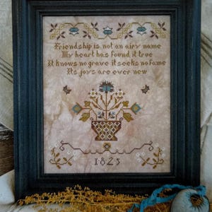 May include: A framed cross-stitch sampler featuring a floral basket motif and the text: Friendship is not an airy name, My heart has found it true, It knows no grave it seeks no fame, Its joys are ever new, with the year 1825 stitched at the bottom.