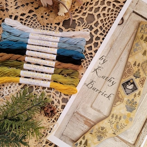May include: A close-up of a cross-stitch pattern for a Christmas stocking with the text "Merry Christmas" and "by Kathy Barrick". The pattern is on a wooden background and includes a variety of colors, including brown, white, and blue.