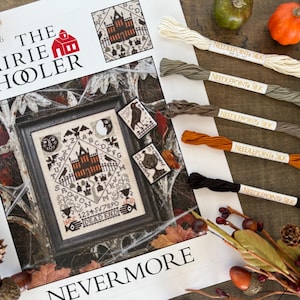 May include: A cross-stitch pattern book titled "The Prairie Schooler" with a spooky Halloween theme. The design features a haunted house, bats, and the words "Nevermore" and "Dead End." Several skeins of silk thread in various colors are also visible.