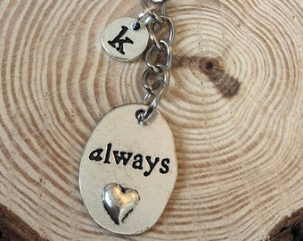 May include: Silver keychain with a small heart charm and an oval charm that says "always". The keychain also has a small round charm with the letter "K" on it.