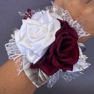 May include: A white and burgundy satin rose wrist corsage with silver and clear rhinestones and lace accents.