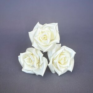 May include: Three ivory satin roses with wire stems. The roses are arranged in a cluster.