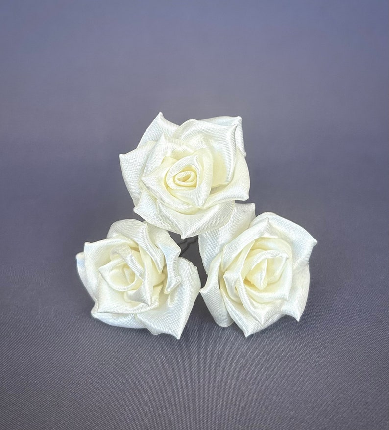 May include: Three ivory satin roses with wire stems. The roses are arranged in a cluster.