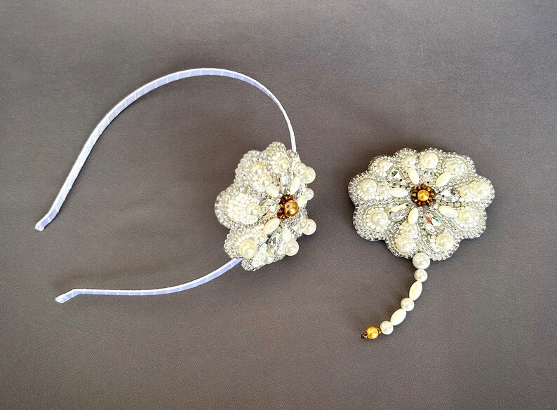 Puede incluir: Una diadema blanca con una flor de perlas y cristales. Un broche a juego de flores de perlas y cristales con una larga cola de perlas.