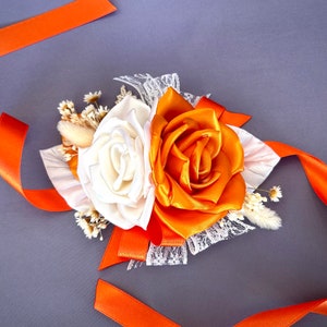 May include: A white and orange silk flower corsage with lace and orange ribbon accents.