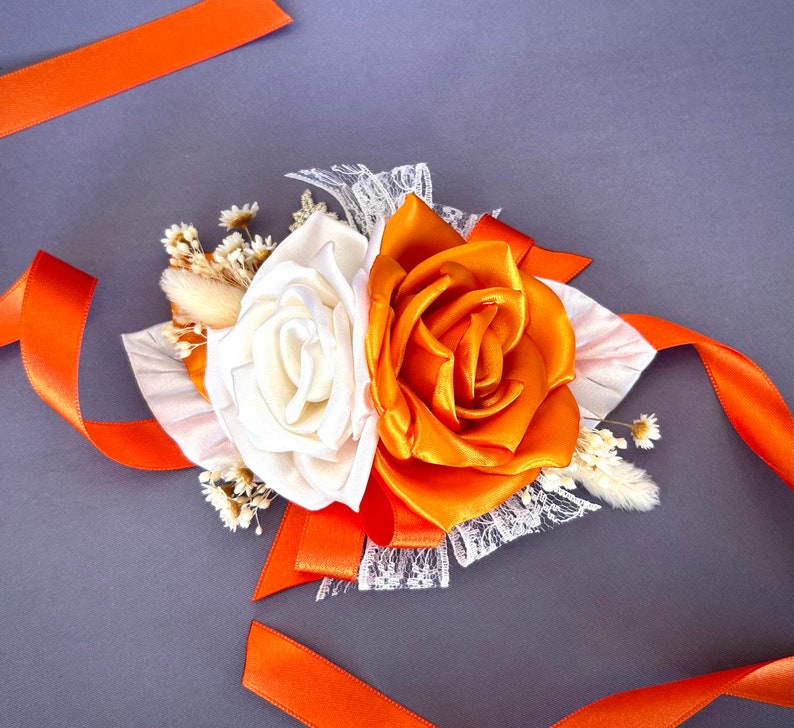 May include: A white and orange silk flower corsage with lace and orange ribbon accents.