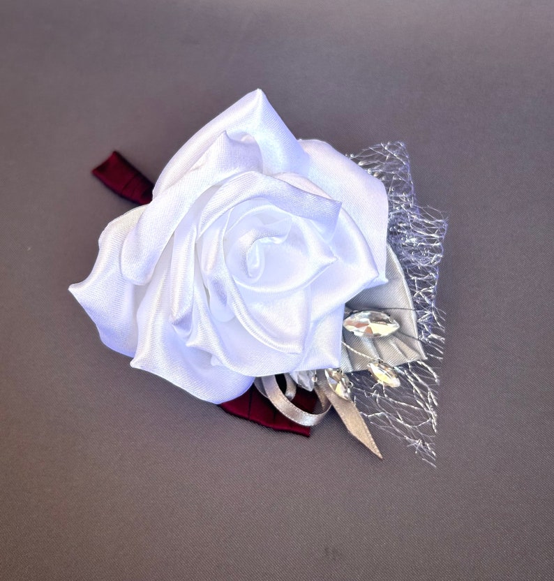 May include: A white satin rose boutonniere with a silver mesh and rhinestones.
