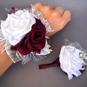 May include: A white and burgundy satin rose wrist corsage with silver lace and rhinestones. A matching boutonniere with a single white satin rose is also included.