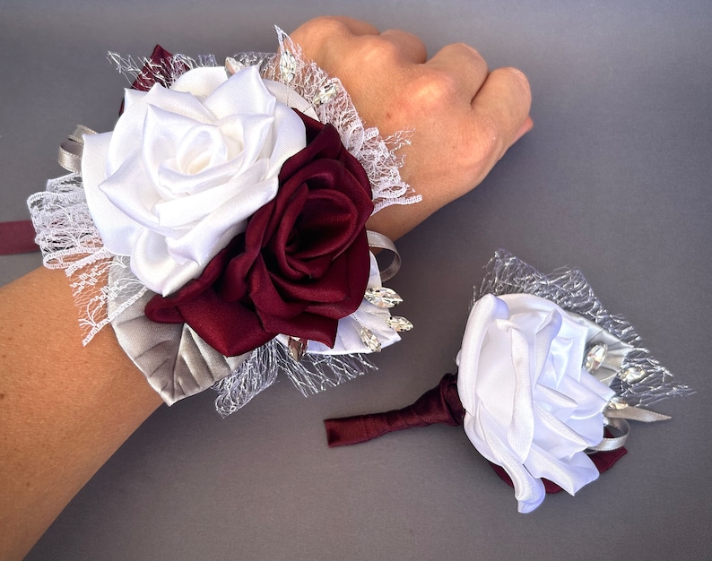 May include: A white and burgundy satin rose wrist corsage with silver lace and rhinestones. A matching boutonniere with a single white satin rose is also included.