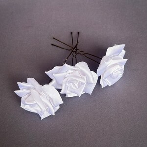 May include: Three white satin rose hair clips with bobby pins. The roses are made of fabric and have a realistic look.