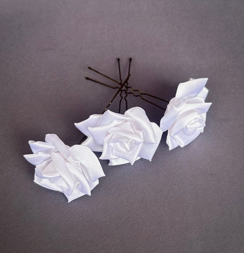 May include: Three white satin rose hair clips with bobby pins. The roses are made of fabric and have a realistic look.