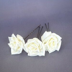 May include: Three white satin rose hair clips with silver bobby pins. The roses are arranged in a row, with the middle rose slightly larger than the other two.