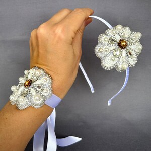 Puede incluir: Dos accesorios para el cabello con forma de flor blanca de cuentas con detalles de perlas. Uno se lleva como pulsera en la mu&ntilde;eca, el otro es una diadema.