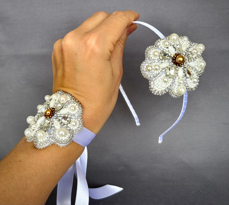 Puede incluir: Dos accesorios para el cabello con forma de flor blanca de cuentas con detalles de perlas. Uno se lleva como pulsera en la mu&ntilde;eca, el otro es una diadema.