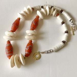 May include: A long necklace made with white and orange beads. The orange beads have a swirling pattern. The necklace has a gold clasp.