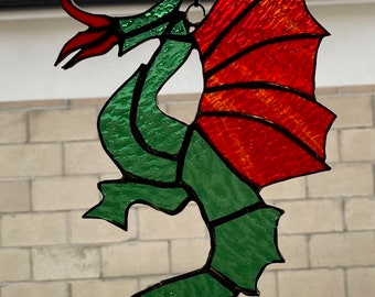 May include: A stained glass dragon with green body, red wings, and white accents. The dragon is hanging from a string.