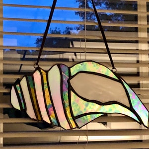 May include: A stained glass seashell window hanging with iridescent green, pink, and purple colors.