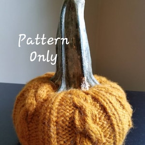 May include: A knitted pumpkin with a cable knit pattern in a mustard yellow colour. The pumpkin has a brown wooden stem. The text "Pattern Only" is written in white on the image.
