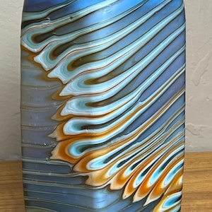 May include: A rectangular glass vase with a blue base and a vibrant orange top. The vase features a swirling pattern of blue, white, and brown colors. The design creates a unique and artistic look, perfect for home decor.