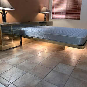 May include: A mirrored bedroom set with a bed frame and matching nightstands. The bed has a light blue mattress. Two black lamps with dark shades sit on the nightstands. The room has tile flooring.
