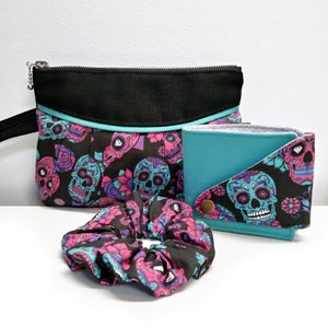 Set de regalo con motivo de calavera y flores, bolsito, carteras y coletero a juego. Estuche para lápices con calaveras en color negro, agua, rosa y morado.