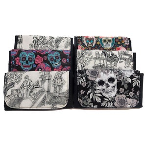 May include: Six different fabric wallets with black trim. The wallets feature various designs including floral patterns, skulls, and a black and white illustration of a couple in a garden.