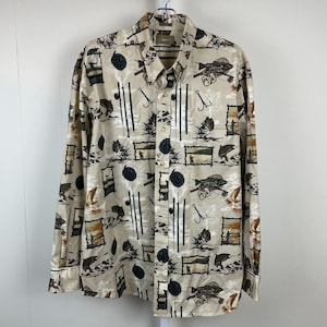 May include: Tan button-down shirt with a fishing-themed pattern. The long-sleeved shirt features illustrations of fish, fishing rods, hooks, and landscape scenes in black, brown, and white. The shirt is hanging on a metal hanger.
