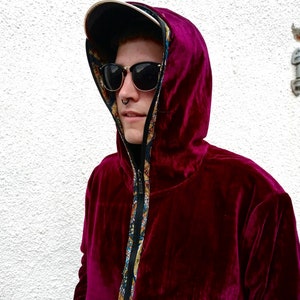 May include: A burgundy velvet hoodie with a zip fastening and a patterned lining. The hoodie has a hood with a drawstring and black trim around the sleeves.