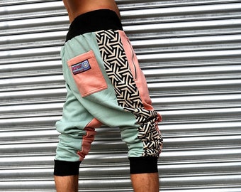 May include: A pair of green, pink, and black patterned pants with a black waistband and a zipper on the side. The pants are cropped and have a loose fit.