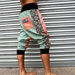 May include: A pair of green, pink and black patterned trousers with a black waistband and a zip on the side. The trousers are cropped and have a loose fit.