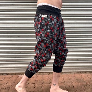 May include: A person wearing black and red patterned pants with a black waistband. The pants have a geometric design with red and gray accents. The person is standing on a brick surface.