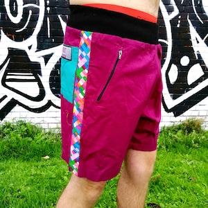 Könnte beinhalten: Burgunderfarbene Shorts mit einem bunten geometrischen Muster an der Seite. Die Shorts haben eine Reißverschlusstasche auf der rechten Seite.