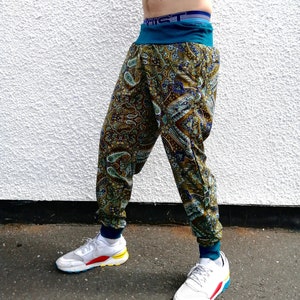 Puede incluir: Un pantalón de estampado paisley verde, azul y dorado con una cintura elástica turquesa. El pantalón se lleva con zapatillas blancas con detalles de colores.