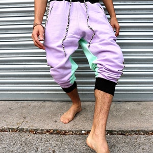 May include: A pair of purple and green sweatpants with black trim and a black waistband. The sweatpants have a unique design with a black and white pattern on the sides.