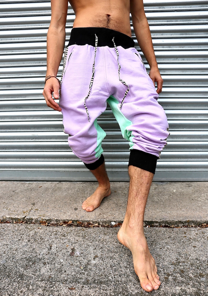 May include: A pair of purple and green sweatpants with black trim and a black waistband. The sweatpants have a unique design with a black and white pattern on the sides.