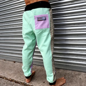 May include: Mint green pants with a black waistband and a purple patch on the back pocket. The pants have a black and white geometric pattern down the side.