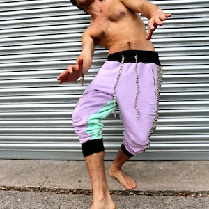 May include: A person wearing a pair of purple, green, and black sweatpants with a black drawstring. The sweatpants have a black and white patterned stripe down the side.