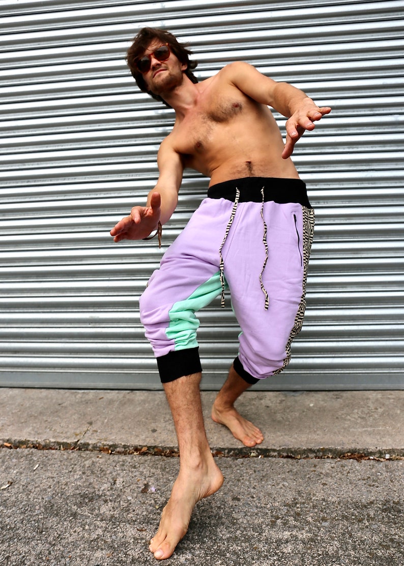May include: A person wearing a pair of purple, green, and black sweatpants with a black drawstring. The sweatpants have a black and white patterned stripe down the side.