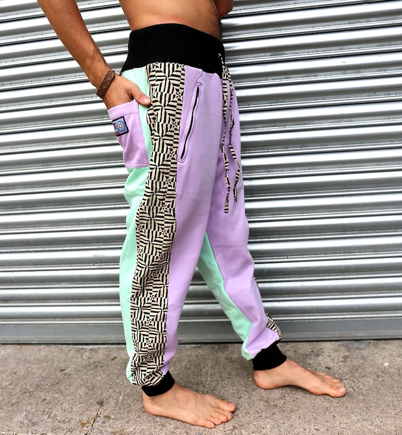 May include: Purple and mint green sweatpants with a black and white geometric pattern on the side. The sweatpants have a black waistband and a drawstring.