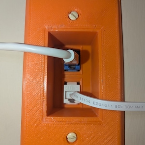 May include: An orange plastic wall plate with two screw holes and a white cable plugged into a blue RJ-45 jack. The cable has the text "AWM 21104 E321011 80C 30V VW-1" printed on it.