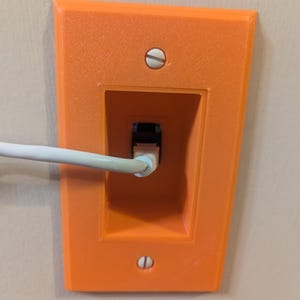 May include: An orange wall plate with a rectangular opening for an Ethernet port. A white cable is inserted into the port. The plate is secured to the wall with two screws.