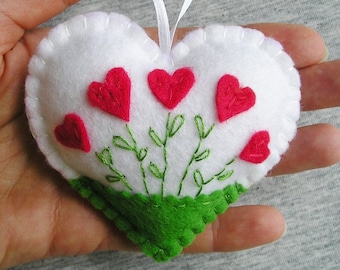 May include: White felt heart-shaped ornament with a green felt base and red embroidered hearts. The ornament has a white ribbon loop for hanging.