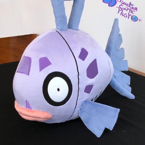 May include: A purple and blue plush toy shaped like a fish with a large eye and a small mouth. The fish has a fin on its back and two fins on its sides. The toy is made of soft, plush fabric and is suitable for children.